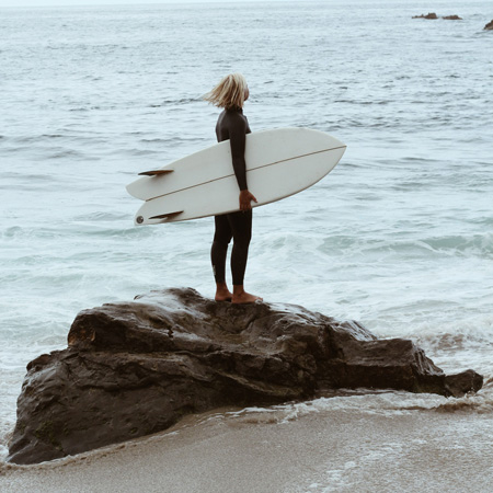 Woman standing on a rock holding a surfboard
